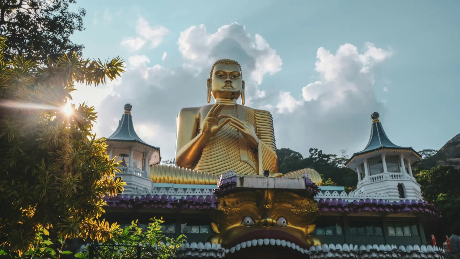 The large seated golden Buddha above the entrance to the Dambulla cave temples, with trees and sky behind