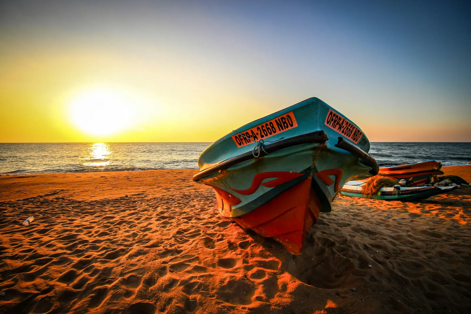 A painted fishing boat resting on the sand at Negombo beach as the sun sets over the sea
