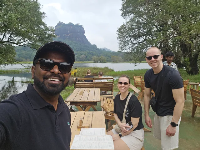 Dhanuka and two guests at a lakeside table, Sigiriya rock behind them