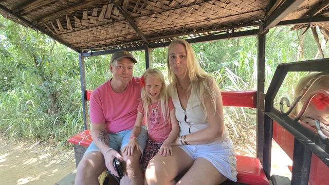 Two guests and a young girl sitting together in an open-sided safari jeep, green bush behind them